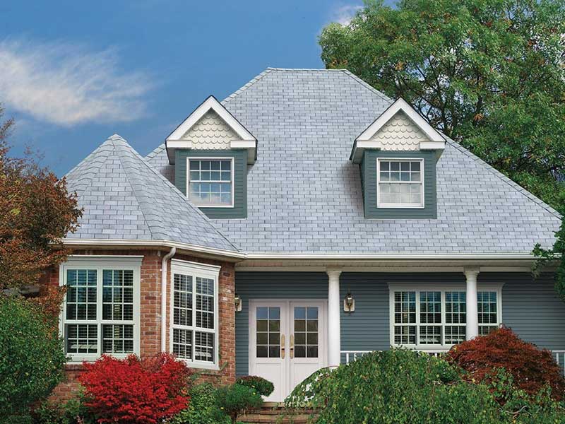 Front view of a home with a gray shingle roof, blue vinyl siding in it's front porch area, and red brick siding on the left next to the front porch